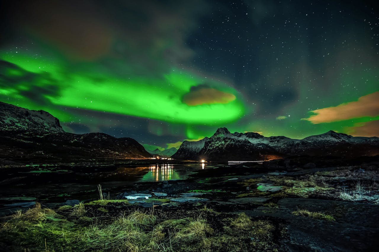 Vibrant aurora borealis illuminating the night sky over a serene mountain and lake landscape.